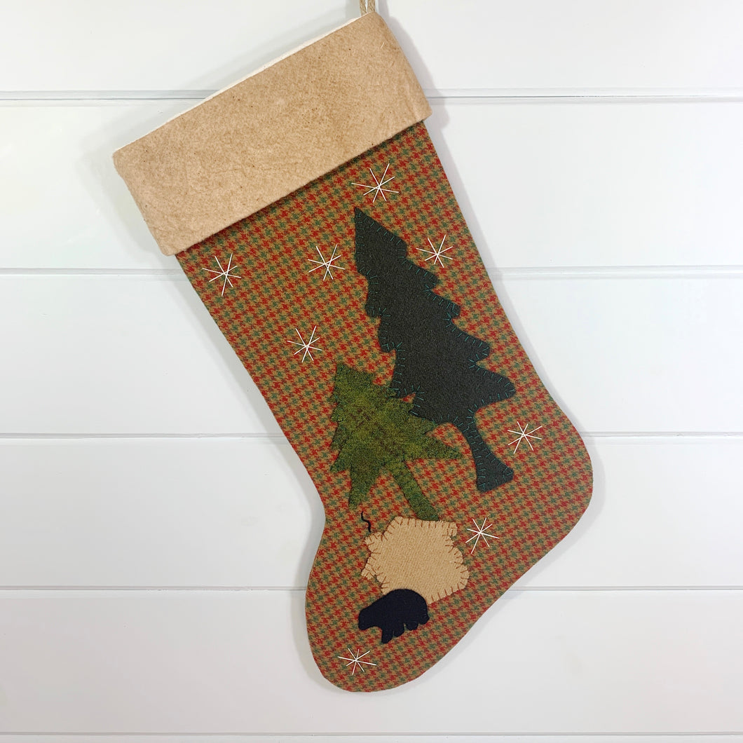 rustic christmas stocking, red, green, gold small plaid wool fabric stocking, ivory snowflakes, two pine trees, tan log cabin, small black bear, woodland christmas stocking, tea dyed cotton batting cuff, large Christmas stocking, bear, cabin and trees are hand stitched to stocking, black stitched curl of smoke coming out of chimney, rustic Christmas stocking