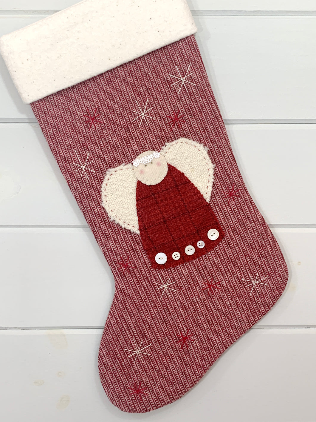 Christmas Angel, red plaid wool dress, off-white wool wings, off-white circular face, dress trimmed with vintage white buttons, red stitching outlining wings, white lace trimmed halo, light brown stitched eyes, pink blush on cheeks, angel hand appliquéd to red herringbone wool Christmas stocking, white and red hand stitched snowflakes, white natural cotton batting cuff