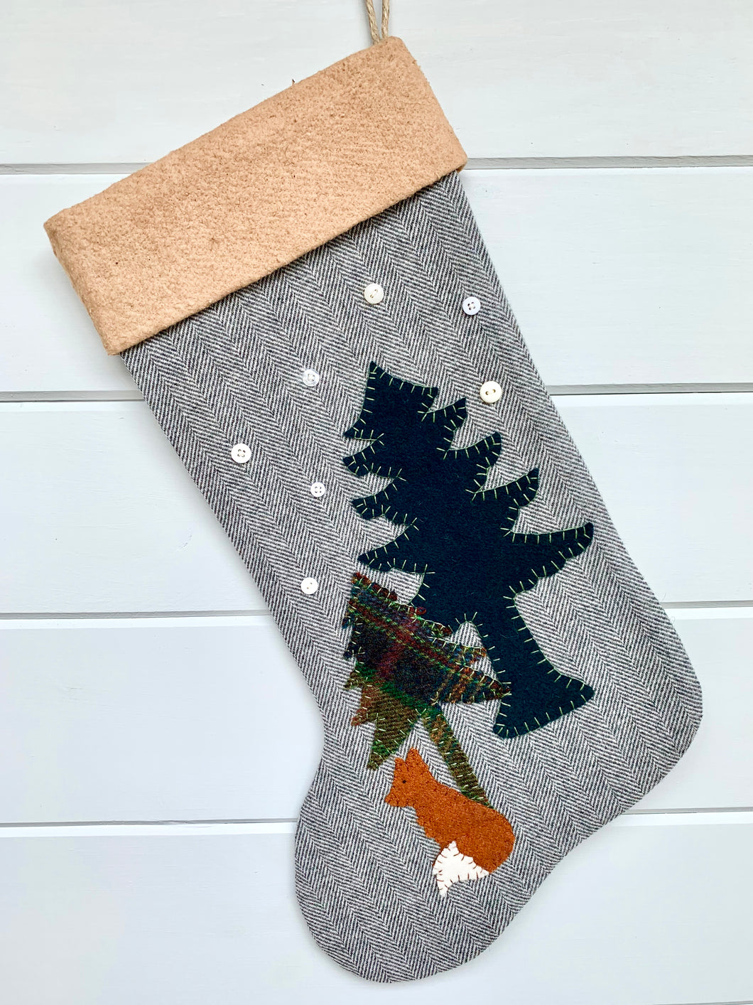 fox Christmas stocking, stocking is gray herringbone wool fabric, tall pine tree is dark green wool fabric, short pine tree is green plaid wool fabric, fox is rustic orange wool fabric with a white wool fabric tip on the tail, black stitching used for eye, trees and fox are hand stitched onto the stocking, white snowflakes are hand stitched on the stocking, cuff is tea dyed cotton batting, woodland fox Christmas stocking, rustic Christmas stocking, large Christmas stocking